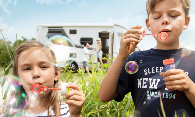To barn som blåser såpebobler i forgrunn av en bobil.